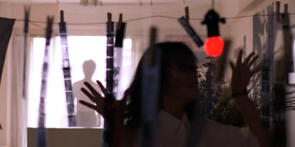 A still image from the 1986 film "Terrorizers", featuring actor Huang Chia-ching standing in front of hanging film strips in a studio apartment
