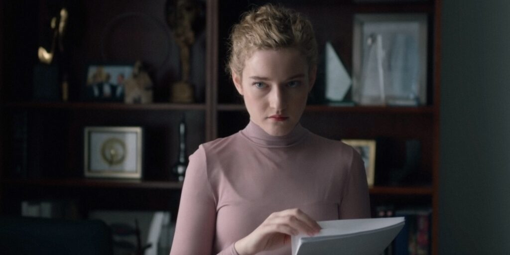 A still image from the film "The Assistant" featuring actor Julia Garner hold a sheaf of papers